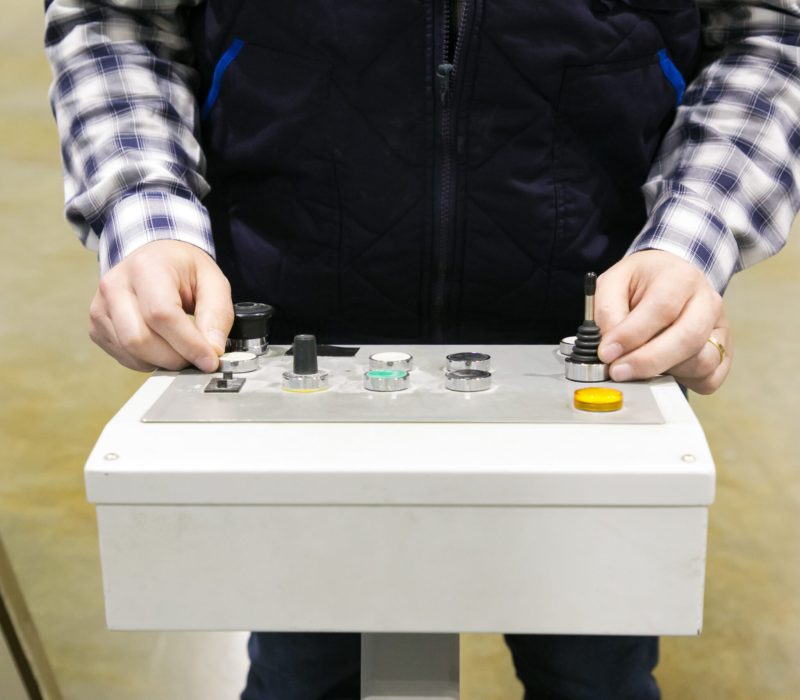 Cropped shot of factory machine operator pressing buttons at control panel. Hands of man working in vest and checkered shirt working at plant. Technology or production process concept